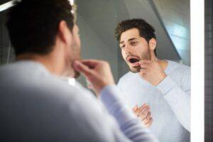 A man brushes his teeth in front of a bathroom mirror.