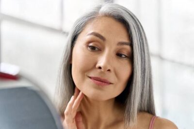 A woman with examines her teeth in a bathroom mirror.